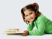 Girl smiling, reading book on floor.